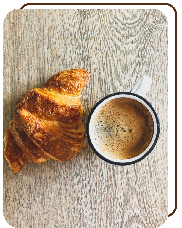 Foto de um croissant junto de uma xícara de café em uma mesa de madeira